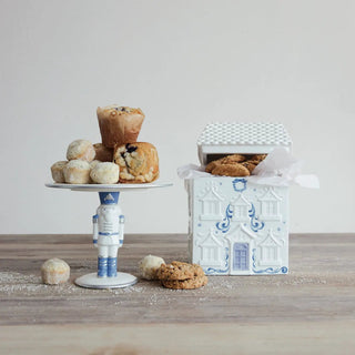 Ceramic house-shaped cookie jar in white and blue with a checkered roof lid, shown beside pastries on a white cake stand.