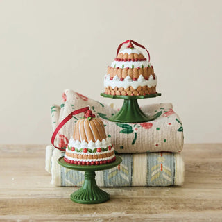 Two resin cake ornaments on green pedestals with white icing, red berries and ribbons