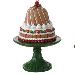 Resin cake on pedestal ornament pair; left brown cake with white icing and red berries, right white-iced cake with berries.