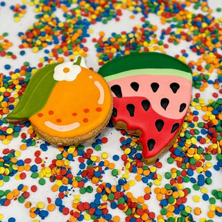 Two fruit-shaped cookies: watermelon slice with green rind and pink flesh; peach-shaped cookie with orange glaze.