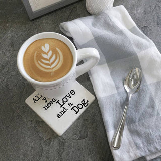 Coaster set of 2 featuring All You Need Is Love and a Dog text beside a coffee mug on a gray countertop