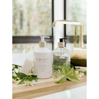 Fresh Linen dish soap on a wooden counter: two bottles, white pump and clear bottle with black pump amid greenery