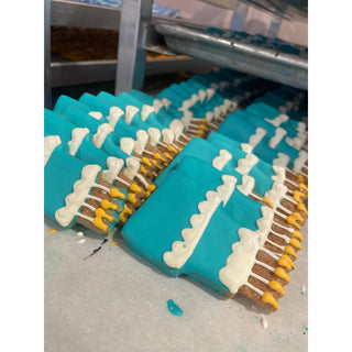 Dog birthday cookies with turquoise fondant and white bone accents on brown biscuits, dozens lined up