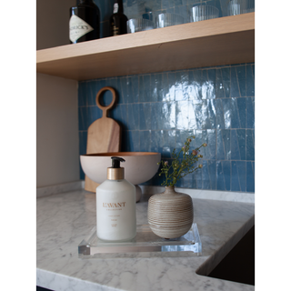 Lucite tray on a marble counter with a white pump lotion bottle and a striped vase