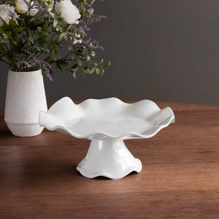 Vida Havana small pedestal cake plate, white ceramic, displayed on a warm wood table beside a vase of flowers