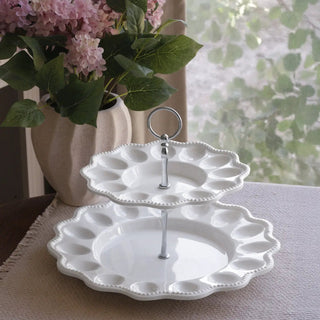 Two-tier white porcelain egg server on a pedestal with scalloped beaded rims and central metal ring handle