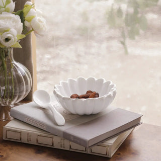 Vienna mini white bowl with spoon, scalloped ceramic, placed on a stack of books beside a glass vase of white flowers
