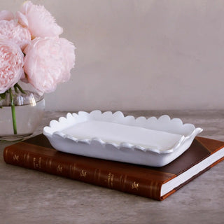 Guest towel holder, white ceramic with scalloped edge, set on a book beside pink peonies.