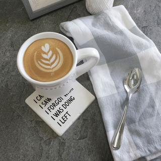 White drink coaster with bold black text reading I can I saw I forgot what I was doing I left beside a mug on gray slate