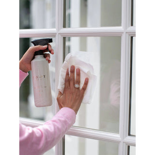 L'AVANT Collective Fresh Linen multipurpose cleaner spray bottle in pink, used to wipe a glass window.