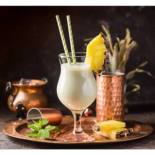Pina Colada wine slushy mix in a hurricane glass with pineapple wedge garnish, mint, and two green-striped straws