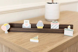 Six 2x2 in wood birthday shapes on a dark display rack: balloon, YAY card, cupcake, gift, cake, cake slice.