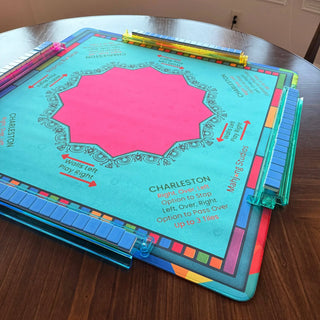 Lunaflor Mahjong Mat with turquoise surface, pink center, rainbow border; translucent blue tile racks.