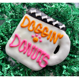 DOGGIN’ DONUTS coffee dog treats; white iced dog treat with orange DOGGIN’ lettering and pink DONUTS icing, bone accents