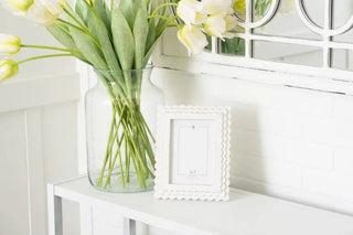 Wood scallop photo frame, white, 5x7 opening, on white shelf beside tulips