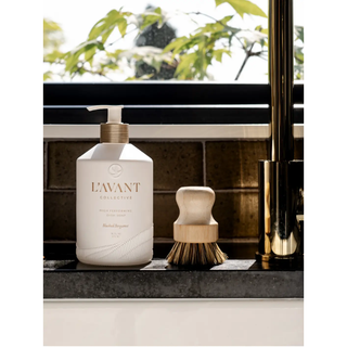 Dish soap white bottle with pump, Blushed Bergamot, brand logo visible, on a bathroom counter beside a wooden brush.
