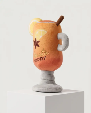 Haute Toddy dog toy, plush drink-mug shaped with orange gradient, lemon slice accent, and gray pedestal base.