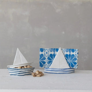 Stoneware sailboat-shaped napkin holder; white ceramic with blue striped napkins.