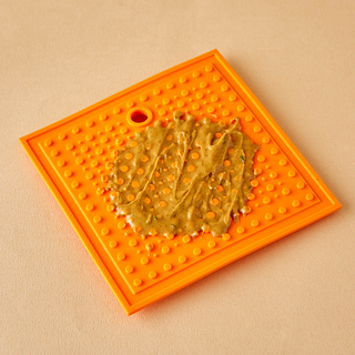 Square orange silicone lick pad for dogs with raised bumps and durable design shown on a tan background