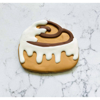 Cinnamon roll cookie with white icing drizzle and brown swirl on tan base