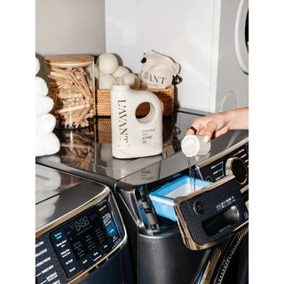 Laundry detergent bottle in cream with built-in handle labeled Fresh Linen being poured into a washing machine.