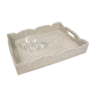 Large cream scalloped rattan tray with handles; woven texture and a glass tumbler on top.