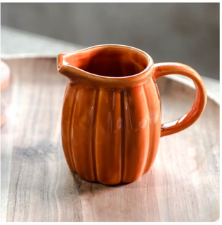 Orange pumpkin-shaped ceramic pitcher with ribbed body and curved handle.