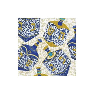 Cocktail napkin featuring blue and gold dreidel pattern on white background.